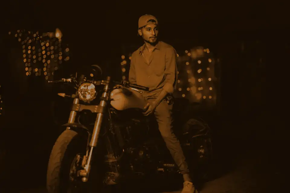 A rider in an orange cap sitting on a motorbike under string lights